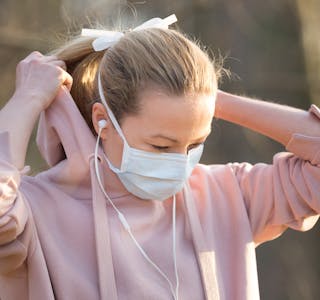 Portrait of caucasian sporty woman wearing medical protection face mask while walking in park, relaxing and listening to music. Corona virus, or Covid-19, is spreading all over the world