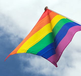 homosexuality, symbolics and gay pride concept - close up of rainbow flag waving on building