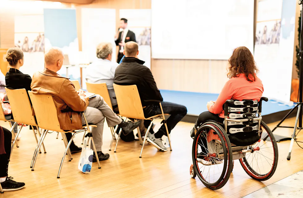 Rear view of nrecognizable woman on a wheelchair participating at business conference talk.